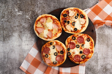 Pizzette or mini-pizza on a round wooden cutting board on a dark grey background. Top view, flat lay