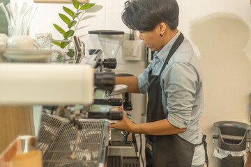 An Asian female barista preparing a hot drink for her customer in a greenery coffee shop. Young...