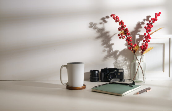 Comfortable workplace with cup of coffee, camera, notebooks and picture frame on white table.