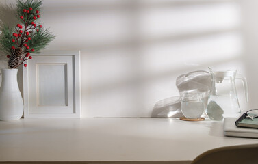 Bright modern workplace with picture frame, glass of water, laptop and notebook on white table.