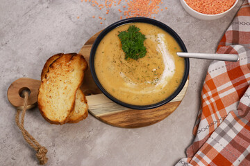 red lentils soup puree in dark bowl with bread on grey marble table