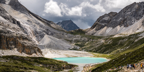 Panorama of the tourists hiking to the Unique colored Milk lake (approx. 4600m altitude) with blue sky and sharp mountains around it - sacred Mt. Chenrezig (6032m). Daocheng Yading, China