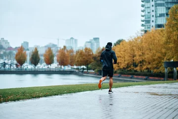 Tuinposter Back view of motivated sportsman jogging in rain. © Drazen