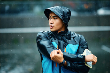 Young athletic man warming up for exercising during rainy day.