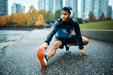 Young athlete stretching his leg during sports training outdoors in rain.