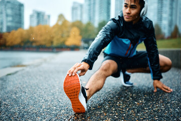 Close up of sportsman doing stretching exercise on road during rainy day. - Powered by Adobe