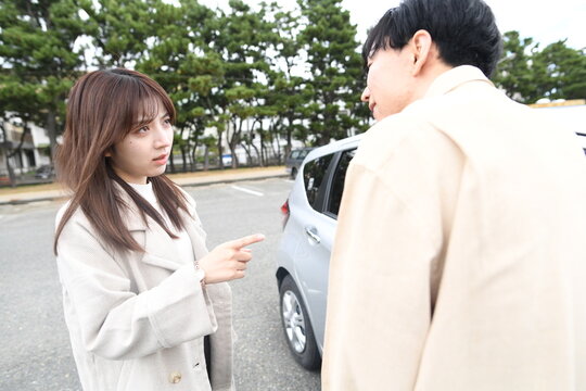 車の前で喧嘩する男女の若いカップル