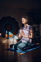 Meditation, zen and elderly woman doing yoga in dark room, shadow and positive energy, balance and mindfulness. Wellness, spiritual and stress relief, calm and peace of mind with fitness and exercise