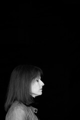 Schwarz Weiss Profil-Portrait einer Frau 50plus am unteren linken Bildrand mit geschlossenen Augen ihrem Gesicht nach rechts vor schwarzen Hintergrund als Textfeld  