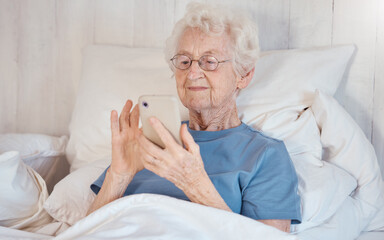 Phone, bed and senior woman in nursing home surfing internet, social media or nostalgic photographs...