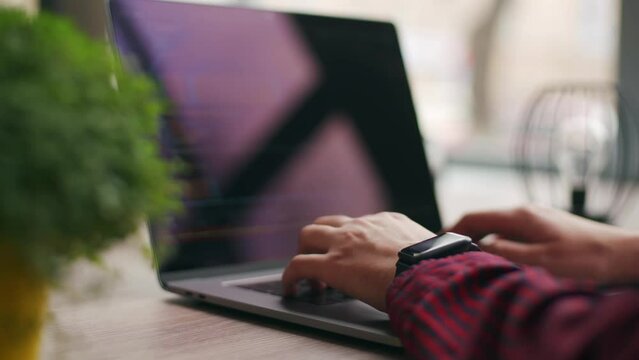 Close up of freelancer's hands typing code on laptop keyboard. Camera slides around developer's figers writing program code on computer display. Programmer working on online application database.