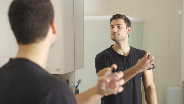 The man is spraying perfume.
Handsome young man looking at himself in the mirror is spraying perfume to smell good.
