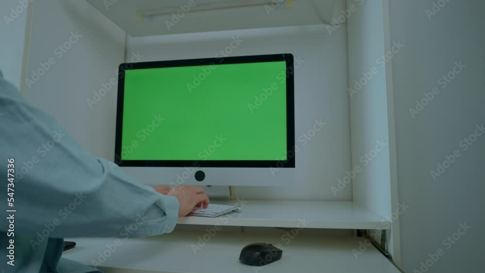 Poster close up details man sitting at the workplace typing on white keyboard monitor with green screen