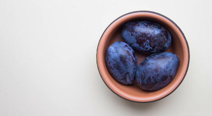Fresh ripe of plums in brown bowl. Top view. Neutral background