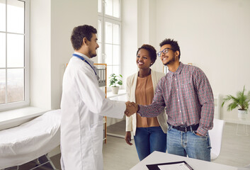 Expectant parents at doctor's consultation. Young couple shakes hands with professional doctor who...