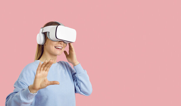 Excited teen gamer girl trying out new VR headset with sensor. Female student on solid pastel pink text space background experiences virtual reality and explores augmented world of education videogame