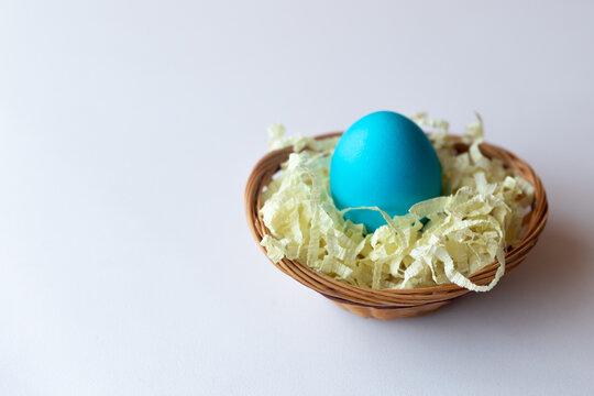 Easter egg painted blue in a basket with artificial straw on white background