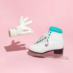 Winter creative layout with skate and mitten holding shoe lace on pastel pink background. 80s or 90s retro aesthetic holiday concept. Minimal season idea.