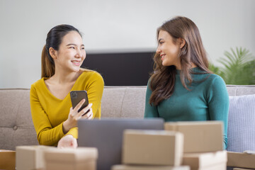 Two Asian women to Startup small business SME entrepreneur of freelance working on laptop computer with parcel box on table laptop at home, online marketing packaging and delivery SME idea concept