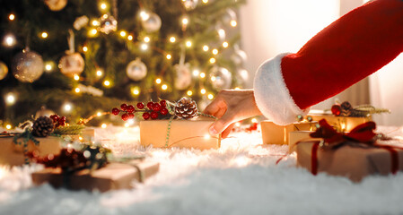 Santa Claus carries Christmas presents under the tre - obrazy, fototapety, plakaty