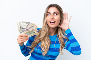 Young Uruguayan woman taking a lot of money isolated on white background listening to something by putting hand on the ear