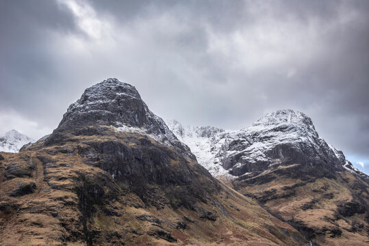 Stunning Winter landscape image of snowcapped Three Sisters mountain range in Glencoe Scottish Highands with dramatic sky