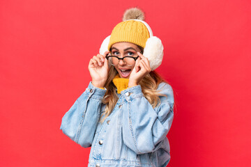 Young pretty Uruguayan woman wearing winter muffs isolated on red background background with glasses and surprised