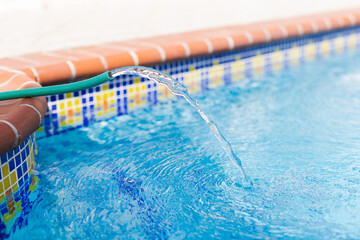 Water pipe filling up swimming pool with clean fresh water, closeup. Pool maintenance. Selective...
