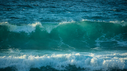 Fototapeta Large Powerful jade turquoise colored waves crashing at Sennen Cove in Cornwall during late sunset obraz