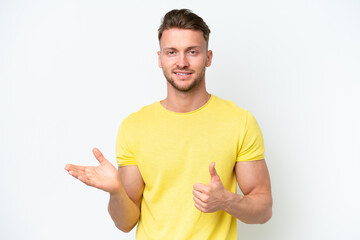 Young blonde caucasian man isolated on white background holding copyspace imaginary on the palm to insert an ad and with thumbs up