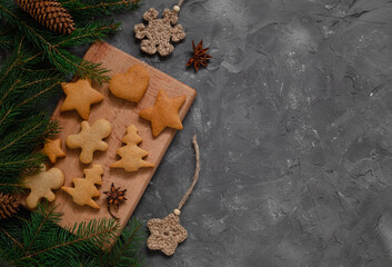 Christmas gingerbread cookies on a wooden board among fir tree branches on a grey background. Copy space.