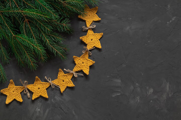Crochet Christmas yellow star garland and fir tree branches on a dark background. Handmade Christmas decor. Copy space.