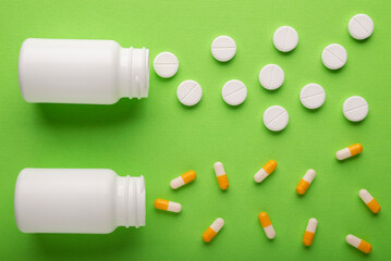 Round tablets and gelatin capsules scattered on a green background. Medicines for diseases and vitamins.