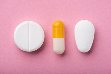 Three tablets on a pink background are different in size and content. Tablets antibiotics, vitamins and dietary supplements.