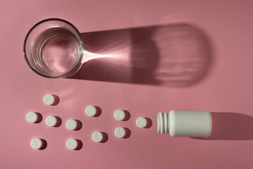 Pills round with water in a glass illuminated by hard light on a pink background. Medicines for oncology.