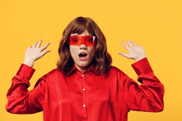 a happy, enthusiastic woman stands on a yellow background in a stylish red shirt and holds her...