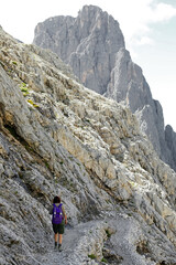 Naklejka premium woman with backpack walks on the gravel path in the italian alps
