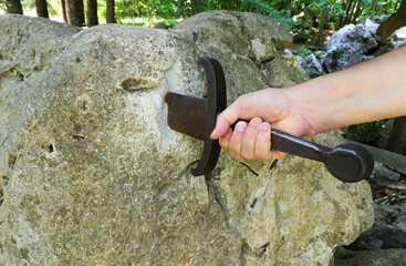 hand of the man who forcibly tries to extract the sword Excalibur is stuck in the rock like King Arthur