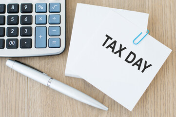tax day inscription on the card on the table next to the pen and calculator, business concept