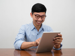 Positive businessman wear glasses using tablet happy smile sit at the desk