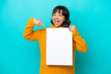 Young latin woman isolated on blue background holding an empty placard with happy expression and pointing it