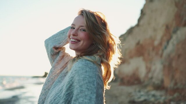 Smiling blonde woman looking at the camera near the beach by the sea