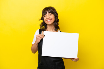 Fototapeta na wymiar Restaurant waiter latin woman isolated on yellow bakcground holding an empty placard with happy expression