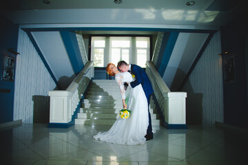 Young beautiful couple in a blue suit and white wedding dress with a bouquet in the hotel