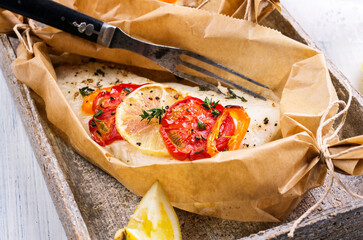 Traditional baked cod fish fillet with vegetable and herbs in backing paper served as close-up on a Nordic design plate - obrazy, fototapety, plakaty