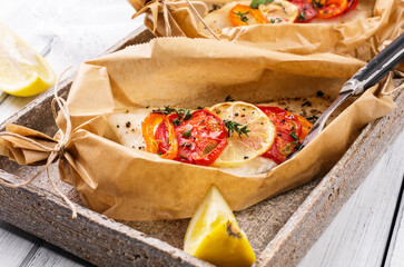 Traditional baked cod fish fillet with vegetable and herbs in backing paper served as close-up on a Nordic design plate