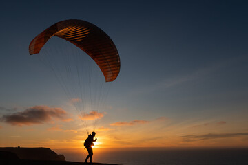 Paraglider flying over thesea shore at sunset. Paragliding sport concept.