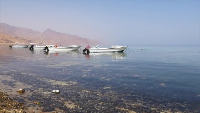 View Of The Seashore With Boats And Distant Mountains In The Calm