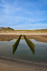 Groyne for the reduction of sand loss on the beach. Landscape shot of pile building in front of dune with grass. Blue sky for copy space.