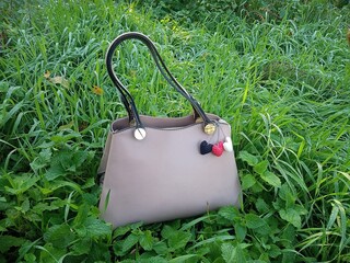 Women's handbag stands on the grass with dew. The object is decorated with knitted hearts.